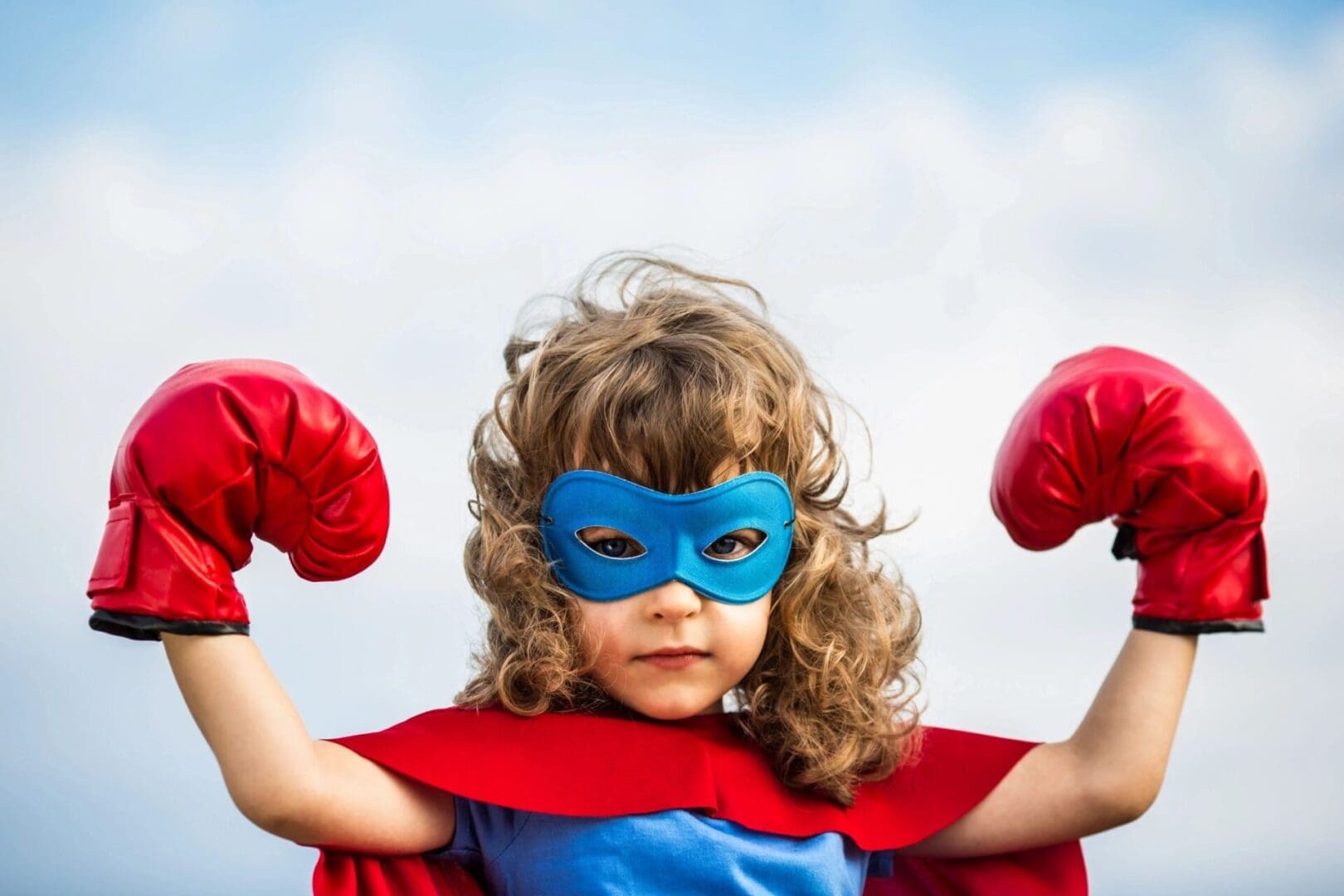 A little girl in a red and blue mask with boxing gloves.