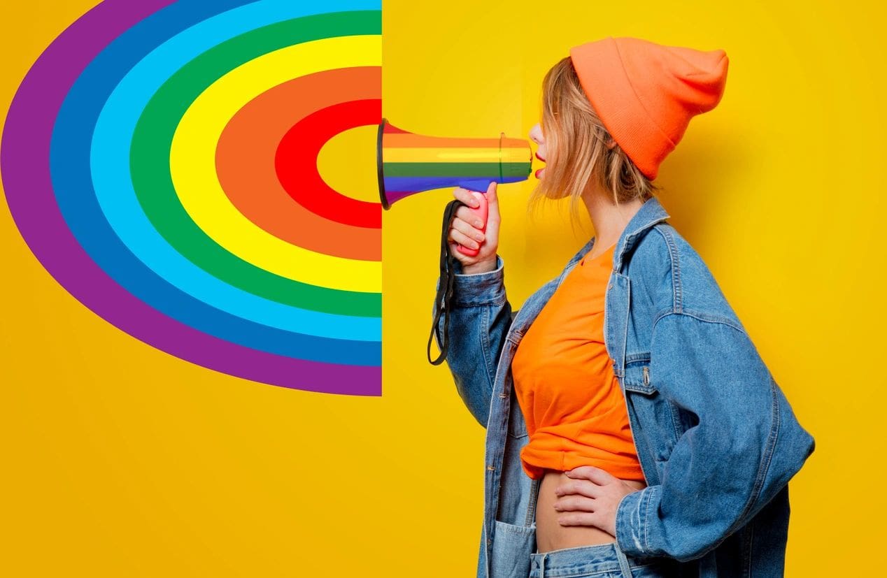 A woman with a megaphone in front of a rainbow wall.